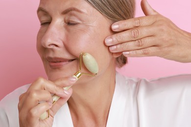 Photo of Beautiful woman doing facial massage with roller on pink background, closeup