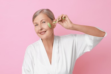 Photo of Beautiful woman doing facial massage with roller on pink background