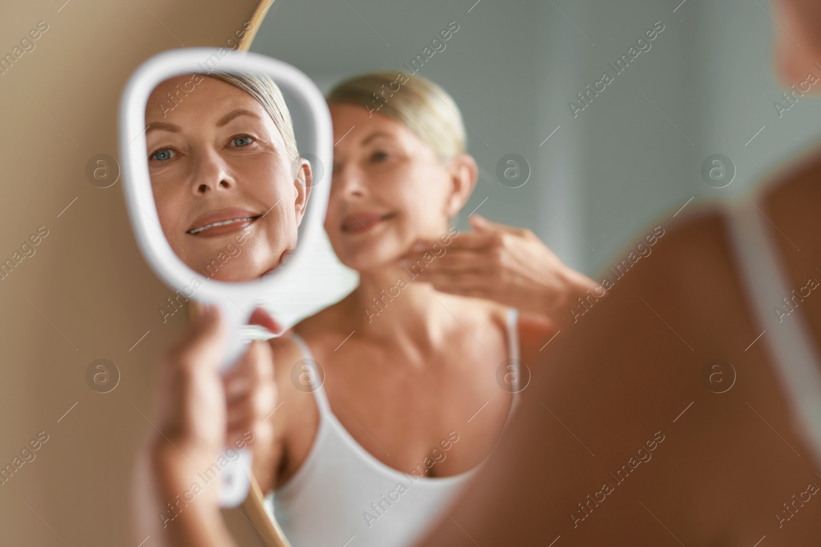 Photo of Beautiful woman doing facial massage near mirror at home