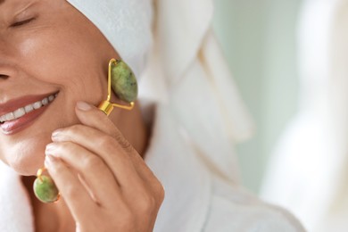 Beautiful woman doing facial massage with roller indoors, closeup