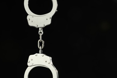 Photo of Metal chain handcuffs on black background, closeup. Space for text