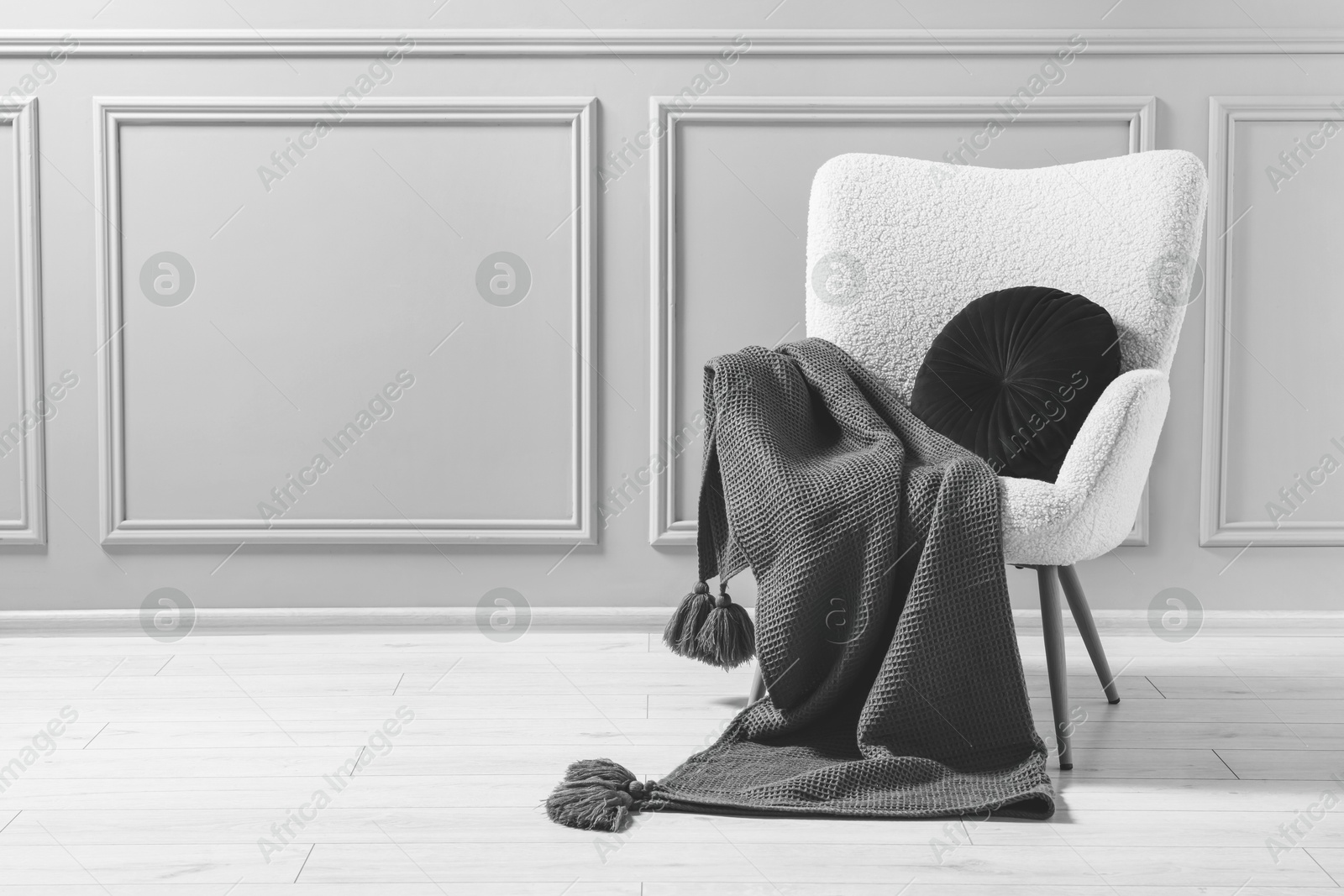 Image of Comfortable armchair with blanket and pillow near wall indoors, black and white