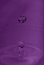 Drop falling into water on purple background, macro view