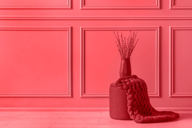 Pouf stool and vase near wall indoors, space for text. Toned in red color