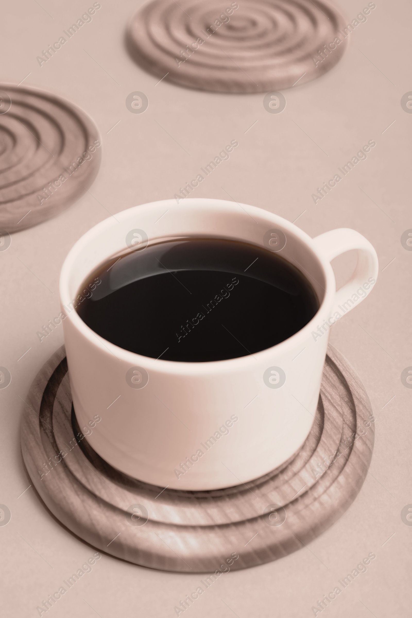 Image of Cup of coffee and stylish wooden coaster on beige background, closeup