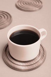 Cup of coffee and stylish wooden coaster on beige background, closeup