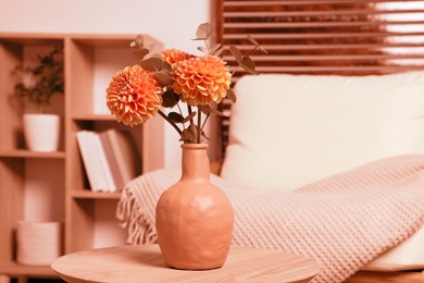 Ceramic vase with beautiful flowers on coffee table near armchair indoors, toned in orange color