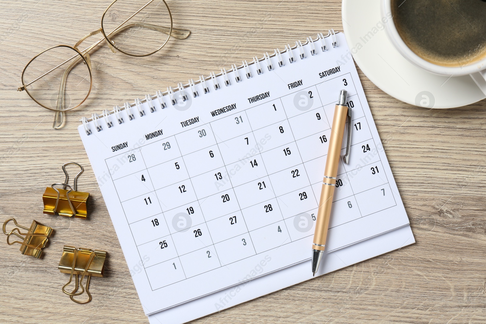 Photo of Timetable. Monthly planner, glasses, coffee, pen and clips on wooden table, flat lay