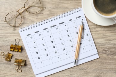 Photo of Timetable. Monthly planner, glasses, coffee, pen and clips on wooden table, flat lay