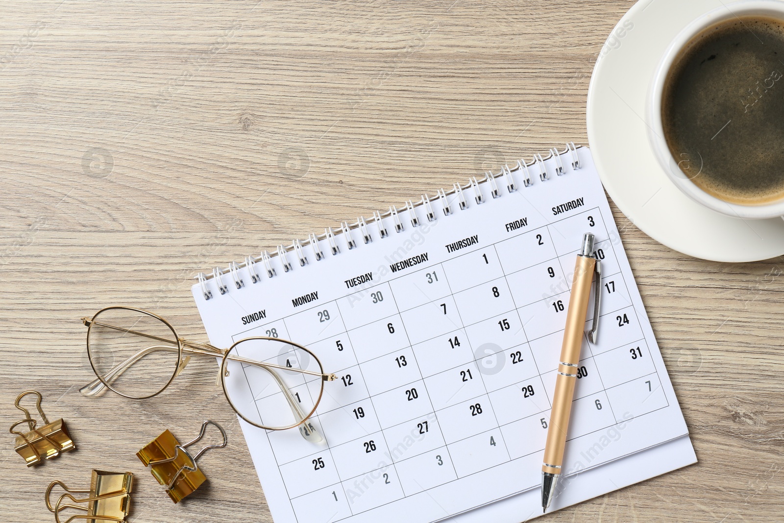 Photo of Timetable. Monthly planner, glasses, coffee, pen and clips on wooden table, flat lay. Space for text