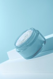 Stylish presentation of face cream in jar against light blue background