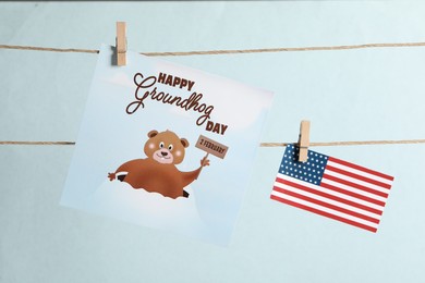 Photo of Happy Groundhog Day greeting card and American flag hanging on light background