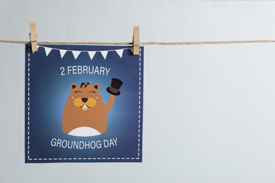 Photo of Happy Groundhog Day greeting card hanging on light background, space for text