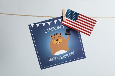 Photo of Happy Groundhog Day greeting card and American flag hanging on light background