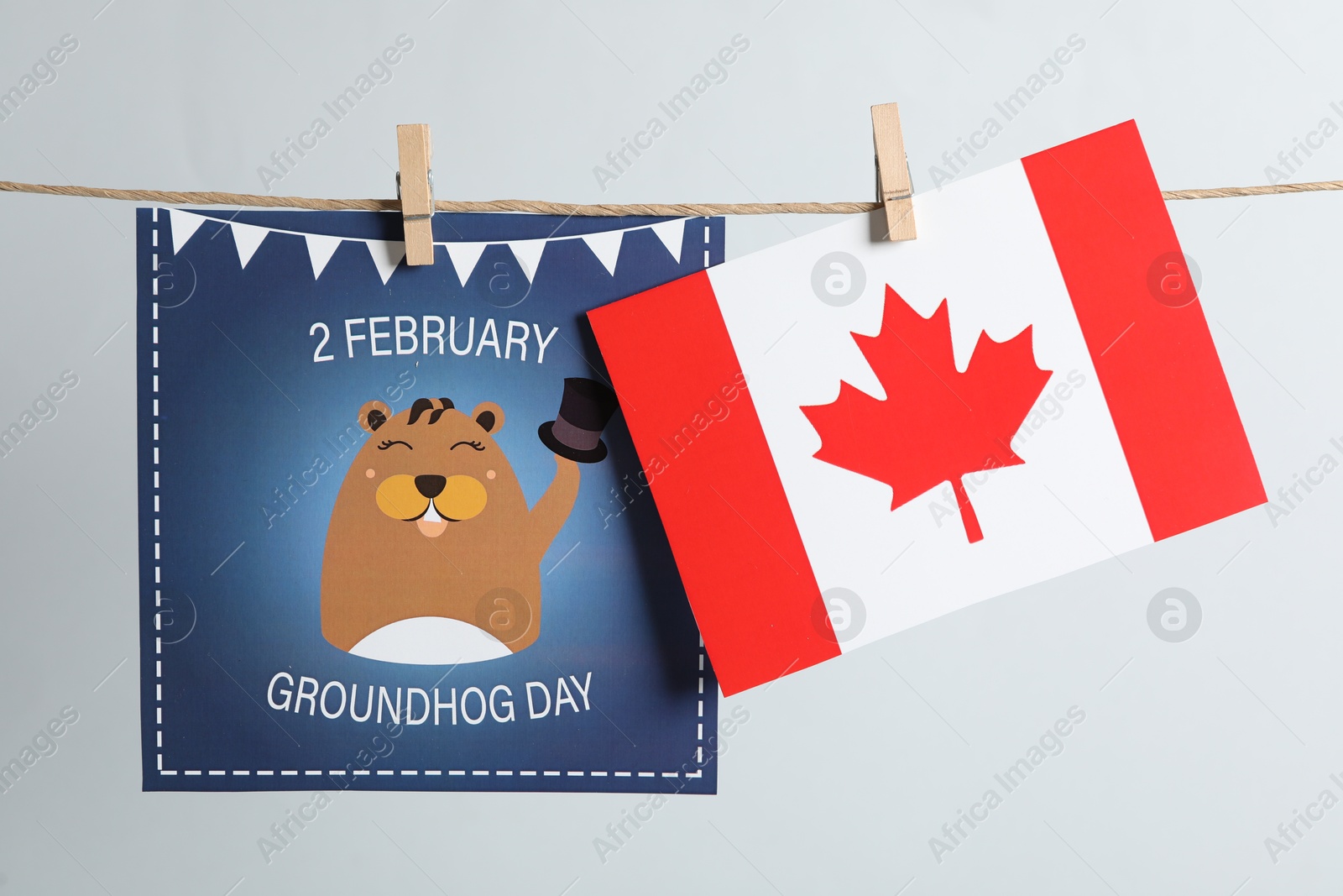 Photo of Happy Groundhog Day greeting card and Canada flag hanging on light background