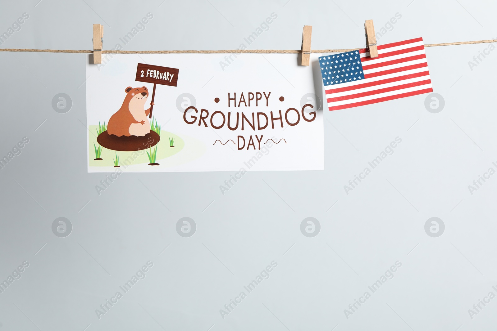 Photo of Happy Groundhog Day greeting card and American flag hanging on light background, space for text