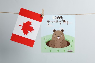 Photo of Happy Groundhog Day greeting card and Canada flag hanging on light background