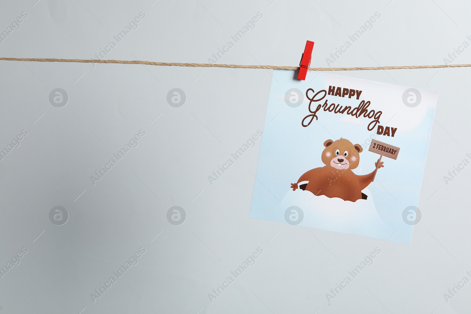 Photo of Happy Groundhog Day greeting card hanging on light background, space for text