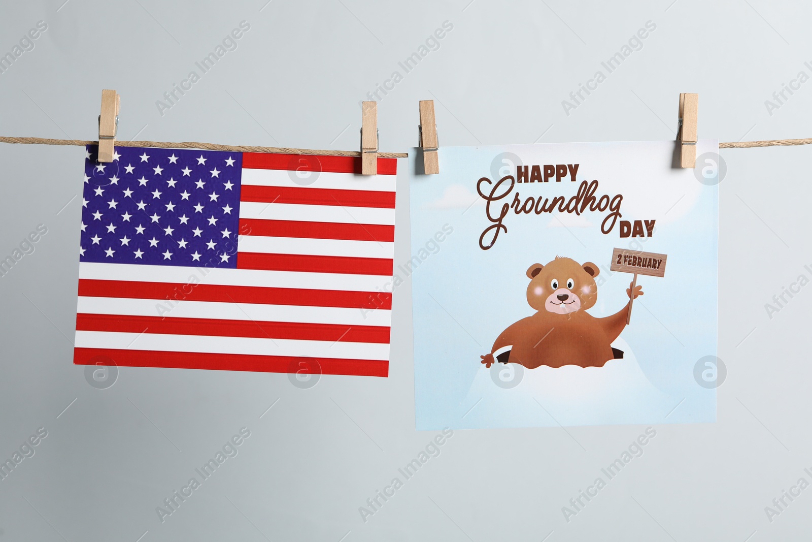 Photo of Happy Groundhog Day greeting card and American flag hanging on light background