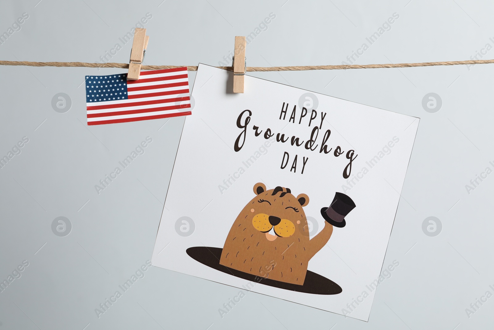 Photo of Happy Groundhog Day greeting card and American flag hanging on light background