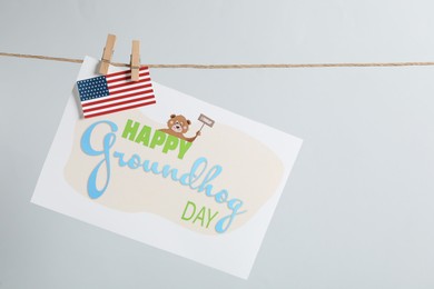 Photo of Happy Groundhog Day greeting card and American flag hanging on light background