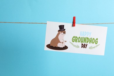 Photo of Happy Groundhog Day greeting card hanging on light blue background, space for text