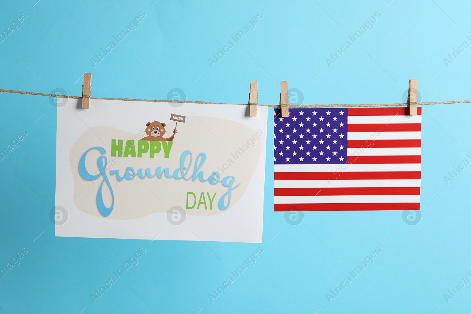 Photo of Happy Groundhog Day greeting card and American flag hanging on light blue background