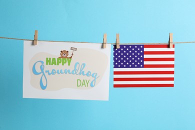 Happy Groundhog Day greeting card and American flag hanging on light blue background