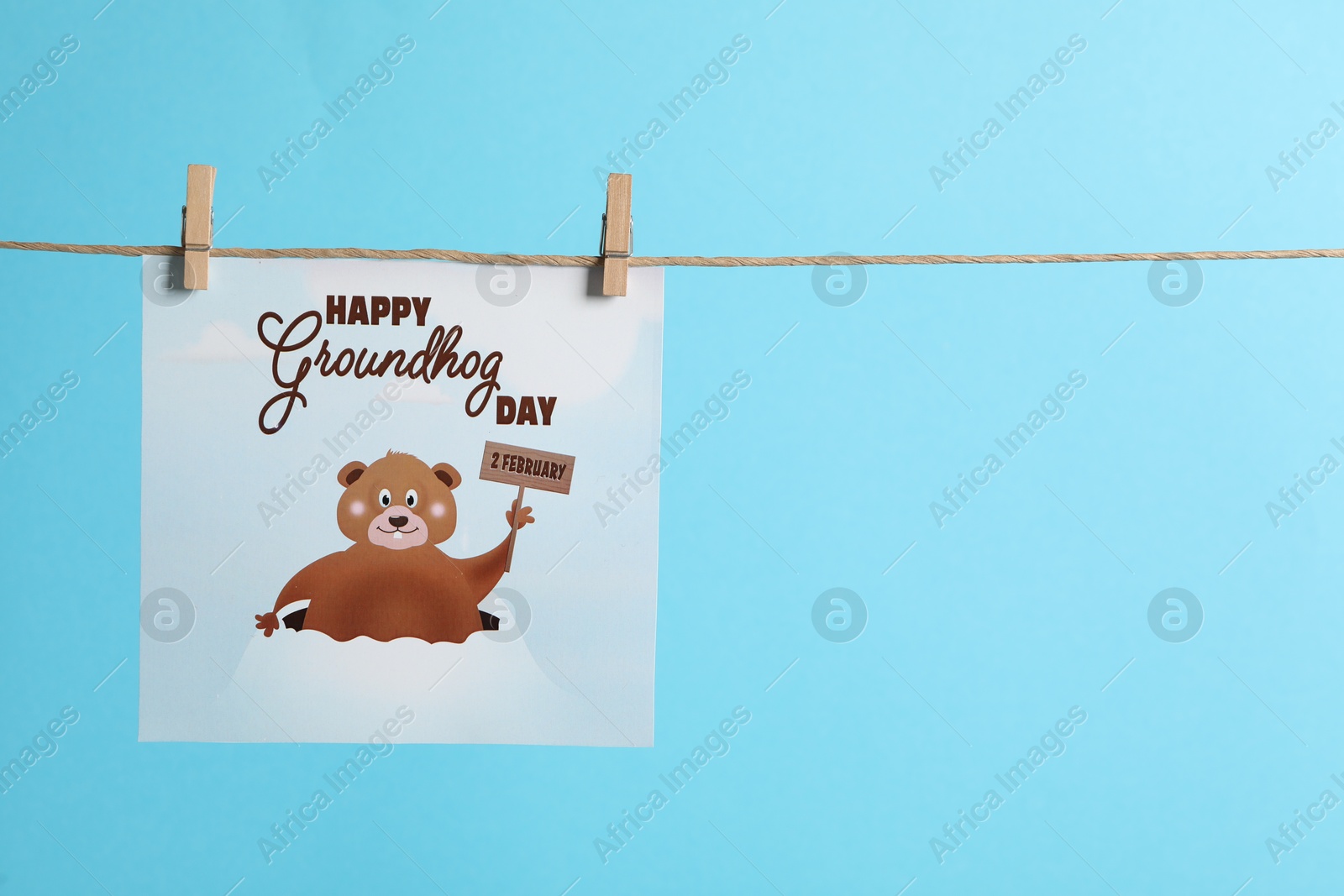 Photo of Happy Groundhog Day greeting card hanging on light blue background, space for text