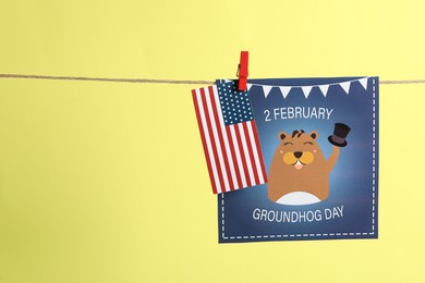 Photo of Happy Groundhog Day greeting card and American flag hanging on yellow background, space for text