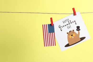 Photo of Happy Groundhog Day greeting card and American flag hanging on yellow background, space for text