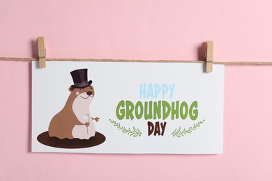 Photo of Happy Groundhog Day greeting card hanging on pink background