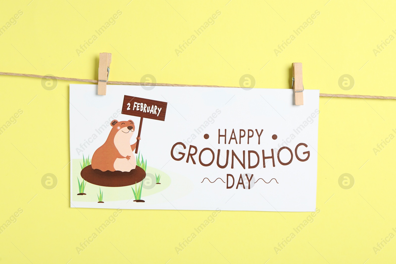 Photo of Happy Groundhog Day greeting card hanging on yellow background