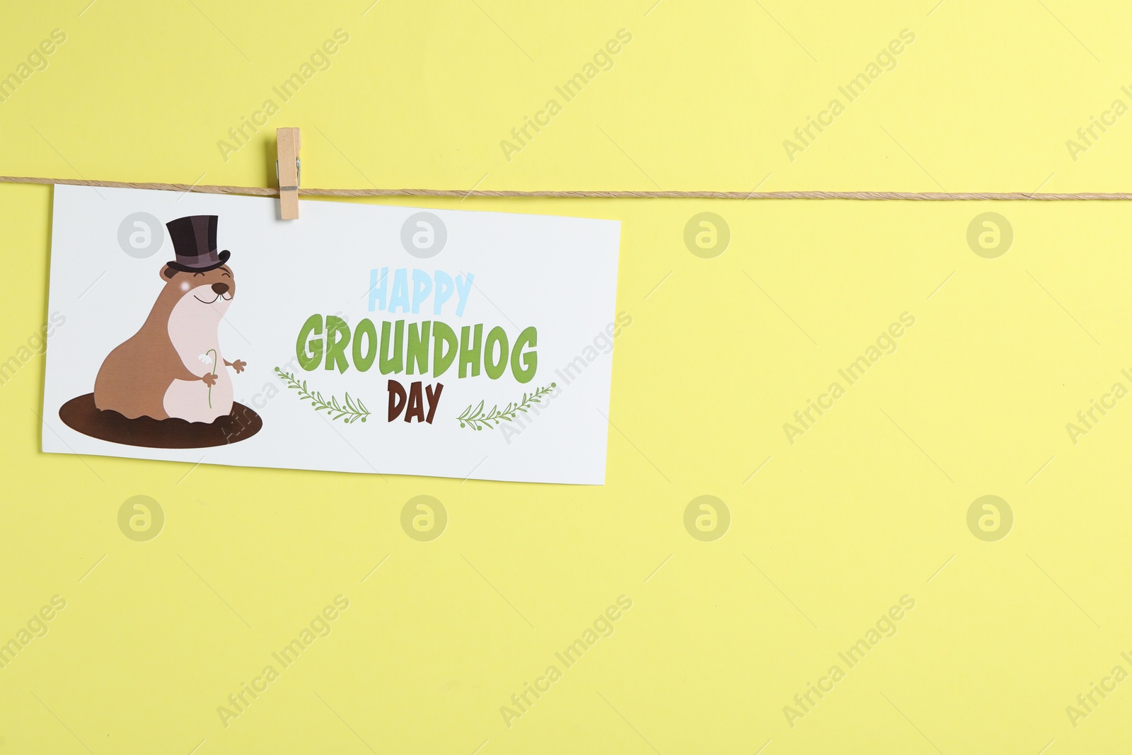 Photo of Happy Groundhog Day greeting card hanging on yellow background, space for text