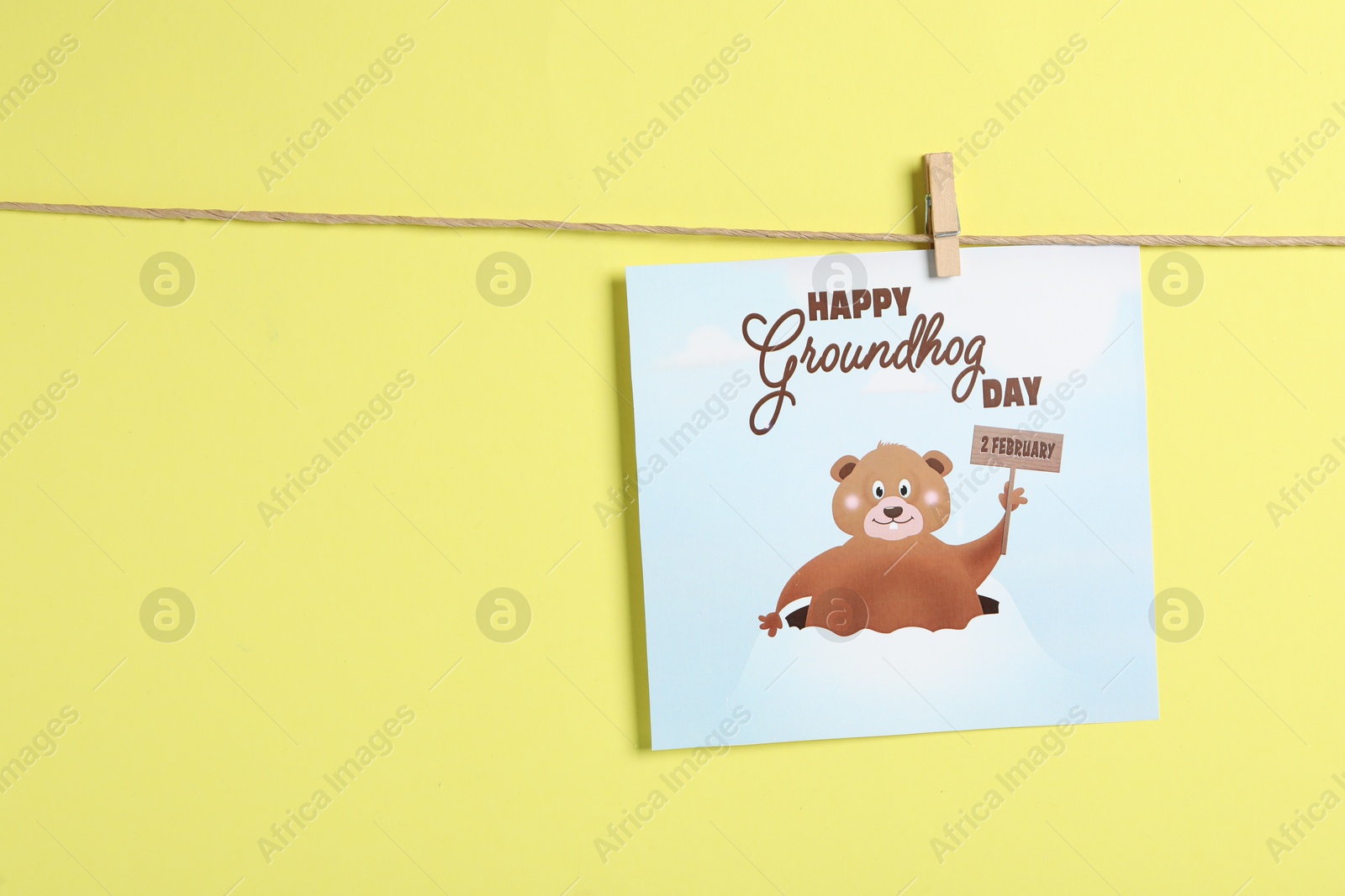 Photo of Happy Groundhog Day greeting card hanging on yellow background, space for text