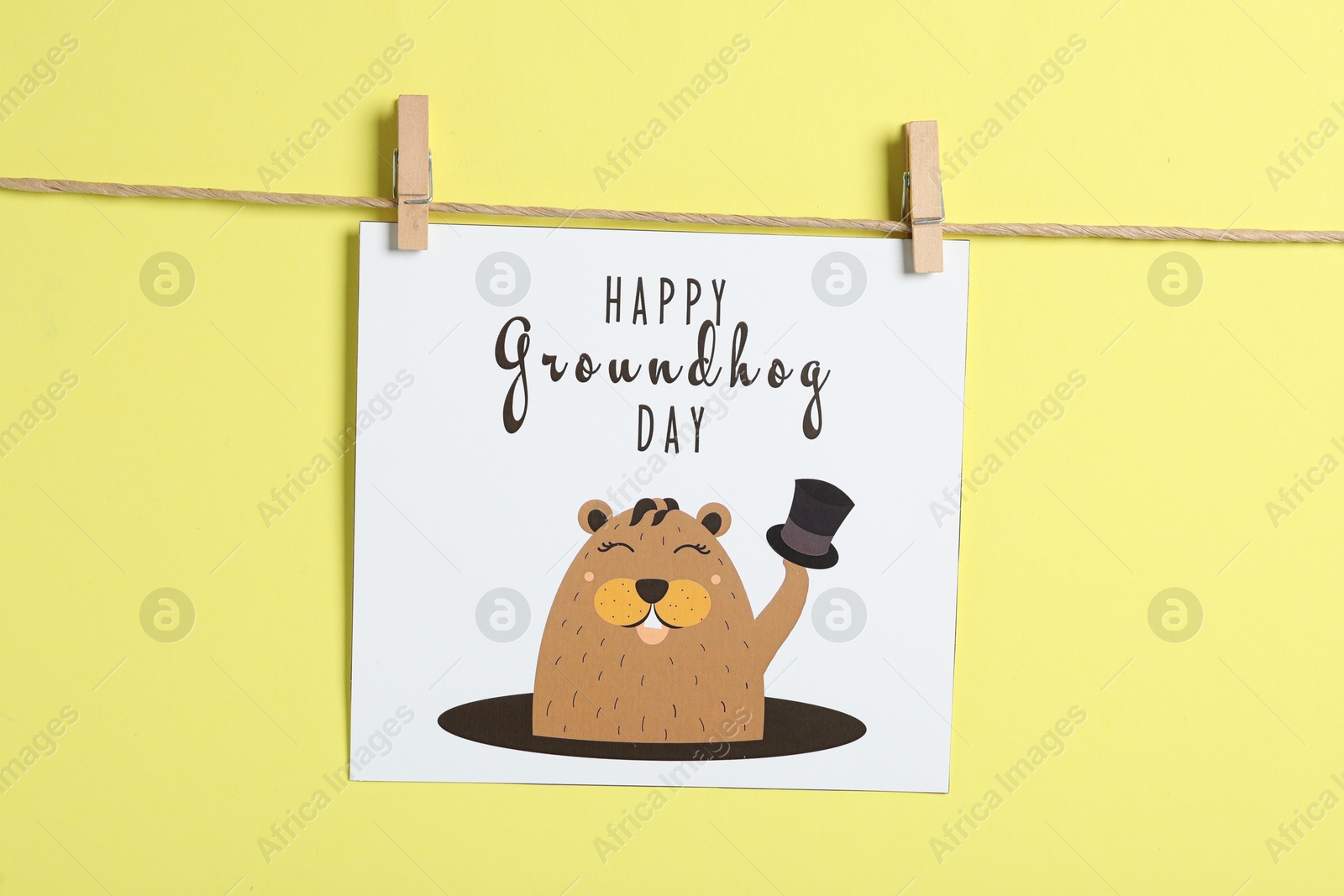 Photo of Happy Groundhog Day greeting card hanging on yellow background