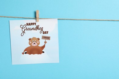 Photo of Happy Groundhog Day greeting card hanging on light blue background, space for text