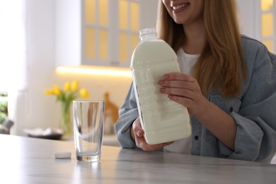 Photo of Young woman pouring milk from gallon bottle into glass at white marble table in kitchen, closeup