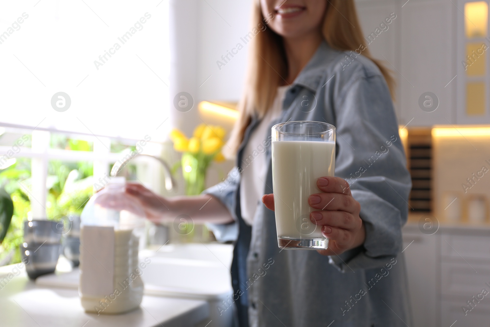 Photo of Young woman with gallon bottle of milk and glass at white countertop in kitchen, closeup