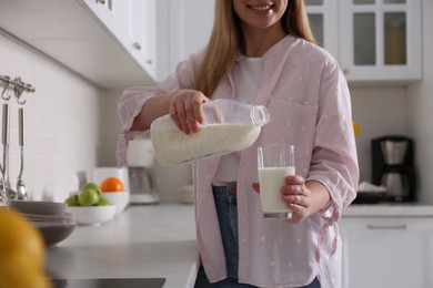 Young woman pouring milk from gallon bottle into glass near light countertop in kitchen, closeup