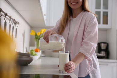 Photo of Young woman pouring milk from gallon bottle into glass at light countertop in kitchen, closeup