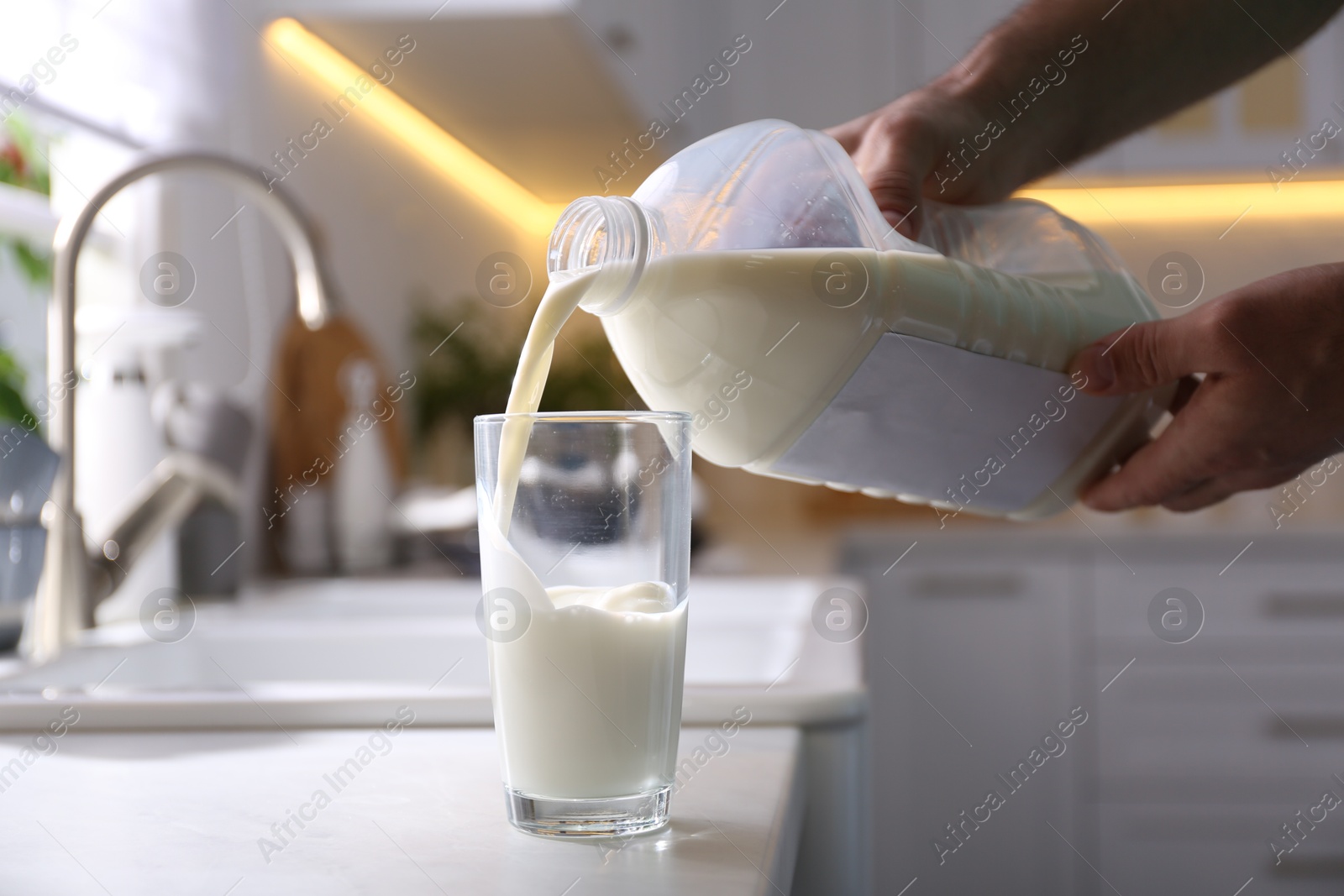 Photo of Man pouring milk from gallon bottle into glass at white countertop in kitchen, closeup