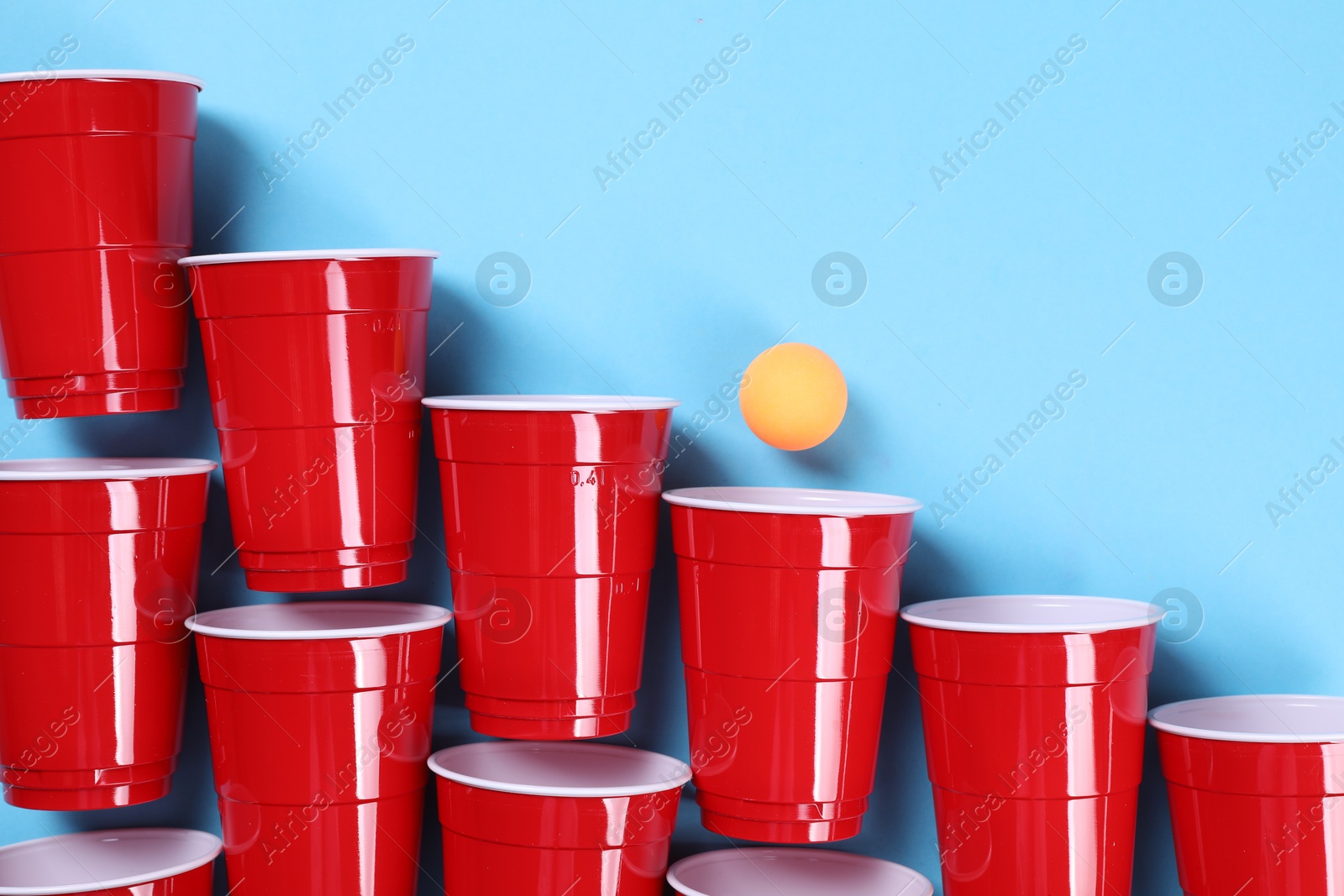 Photo of Plastic cups and ball on light blue background, flat lay. Beer pong game