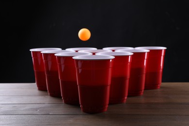 Photo of Plastic cups and ball for beer pong on wooden table against black background