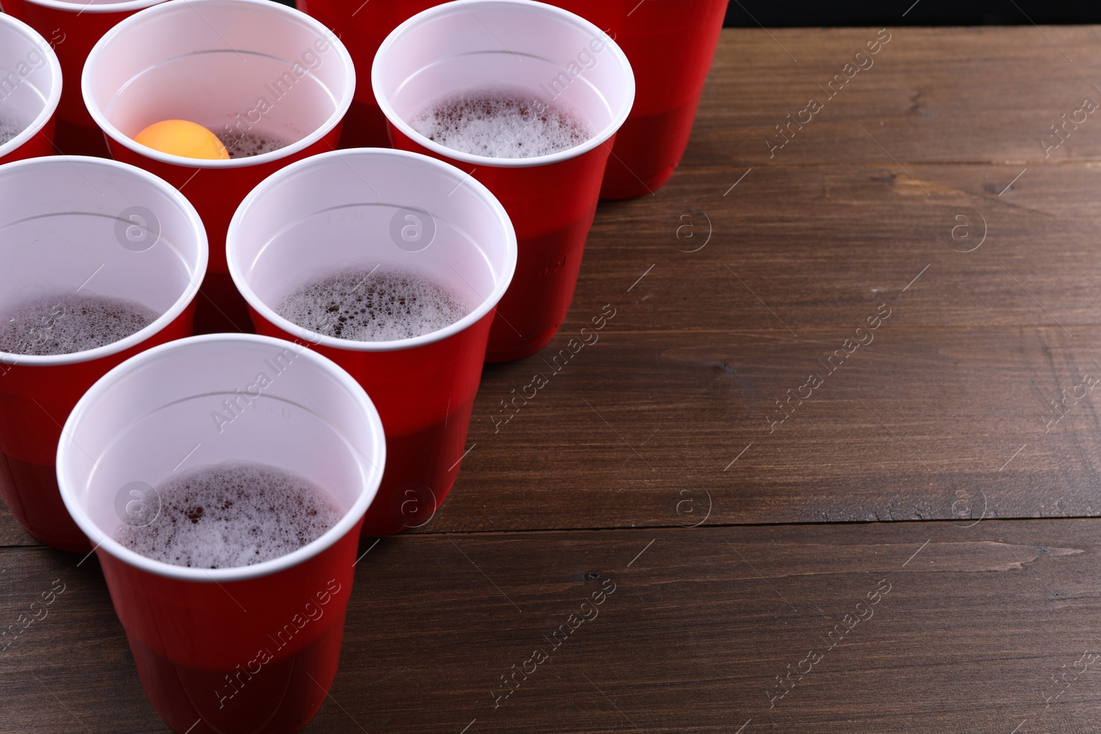 Photo of Plastic cups and ball on wooden table, space for text. Beer pong game