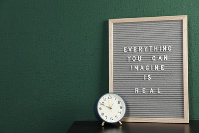 Photo of Letter board with phrase Everything You Can Imagine Is Real and alarm clock on table near green wall. Space for text