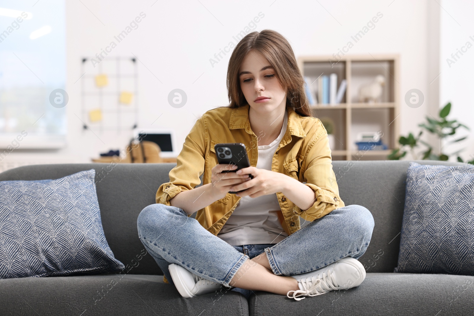 Photo of Loneliness concept. Sad teenage girl using smartphone on sofa at home