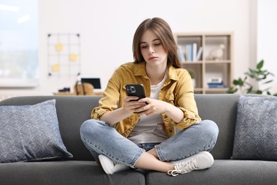 Loneliness concept. Sad teenage girl using smartphone on sofa at home