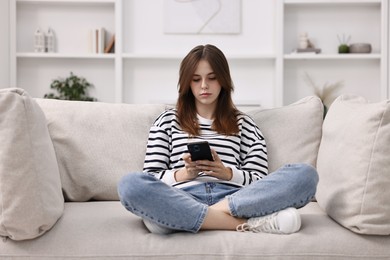 Photo of Loneliness concept. Sad teenage girl using smartphone on sofa at home