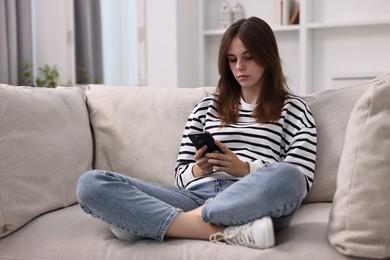 Loneliness concept. Sad teenage girl using smartphone on sofa at home